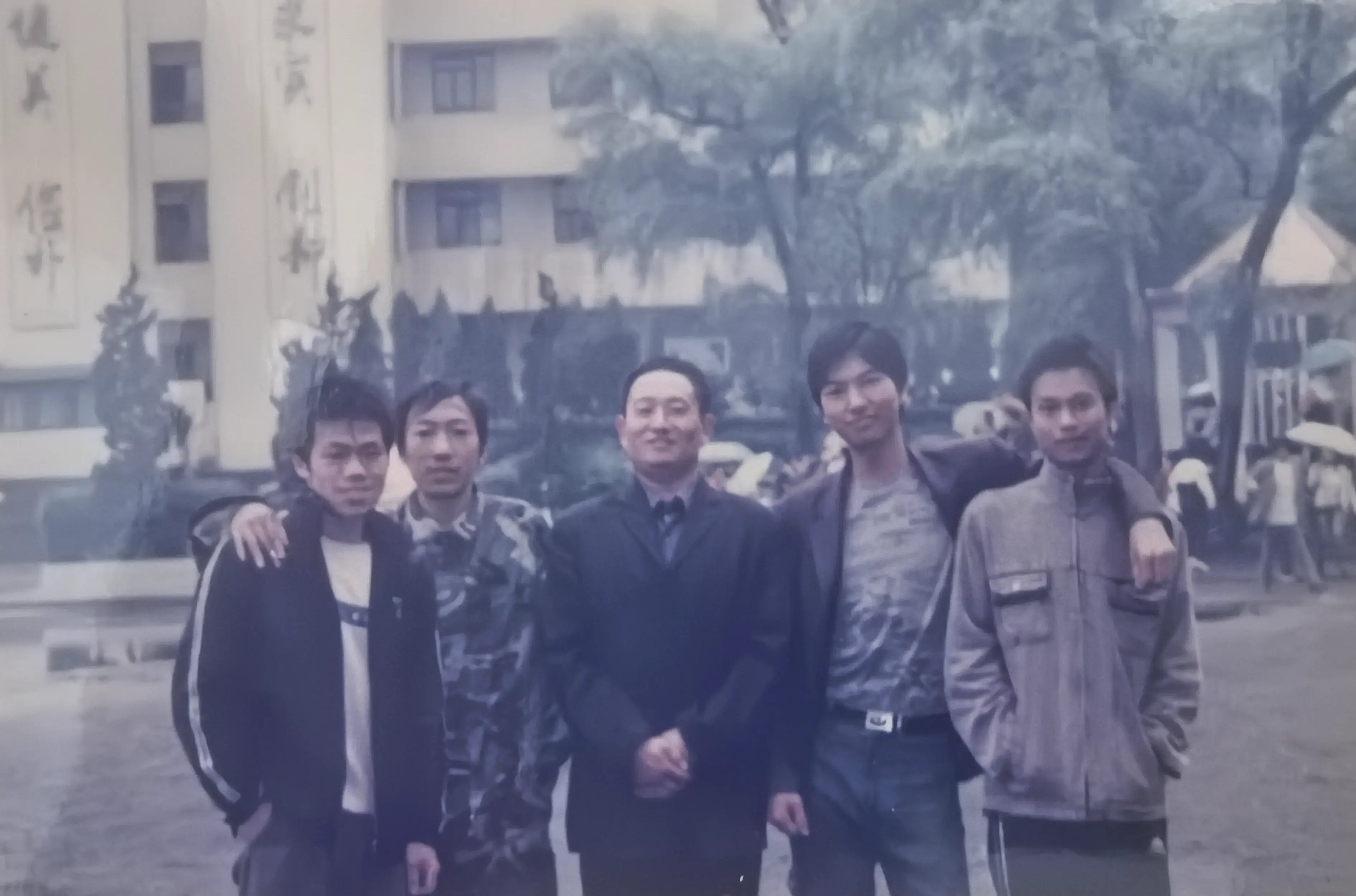 姜南、吴增明、陆云、罗文跟班主任何平老师在教学楼前拍的。四个男生站在何老师身边有点拘谨，何老师倒是笑得很自在。蓝白校服穿了三年，现在看着倒觉得挺好看。
