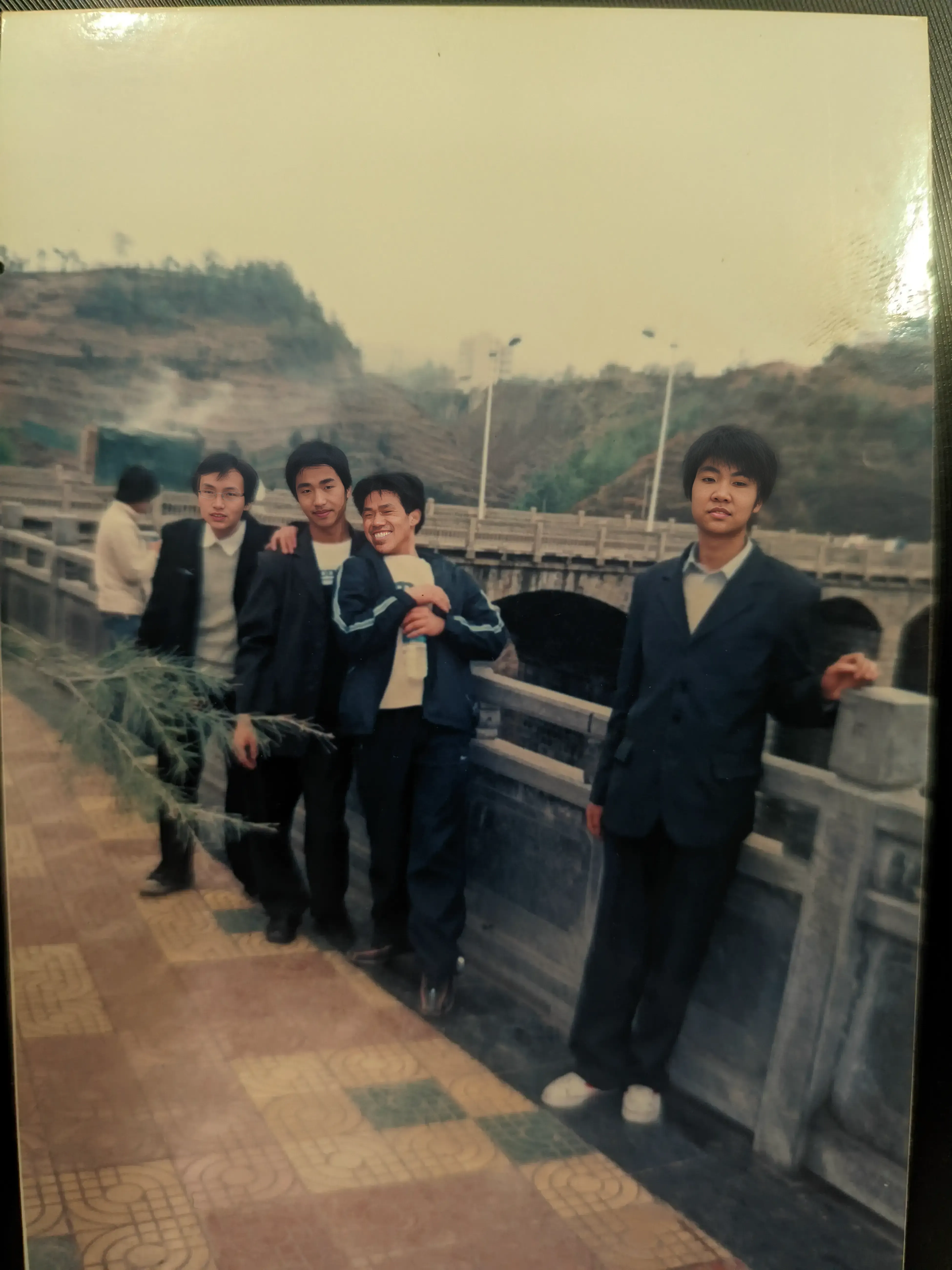 2006年南大桥前，常履华、姜南、高伟、赵建国四位同窗的青春留影，大桥见证了他们高中三年的友谊之路，背景是镇雄熟悉的城市风景。